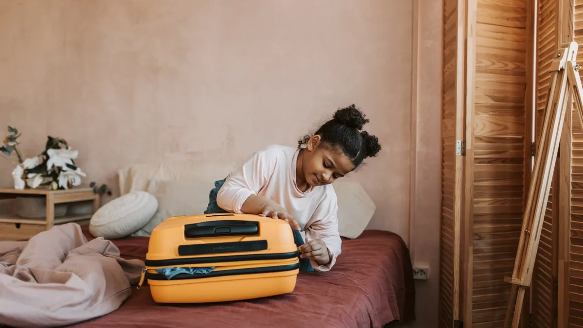 Child packing a yellow suitcase on a bed