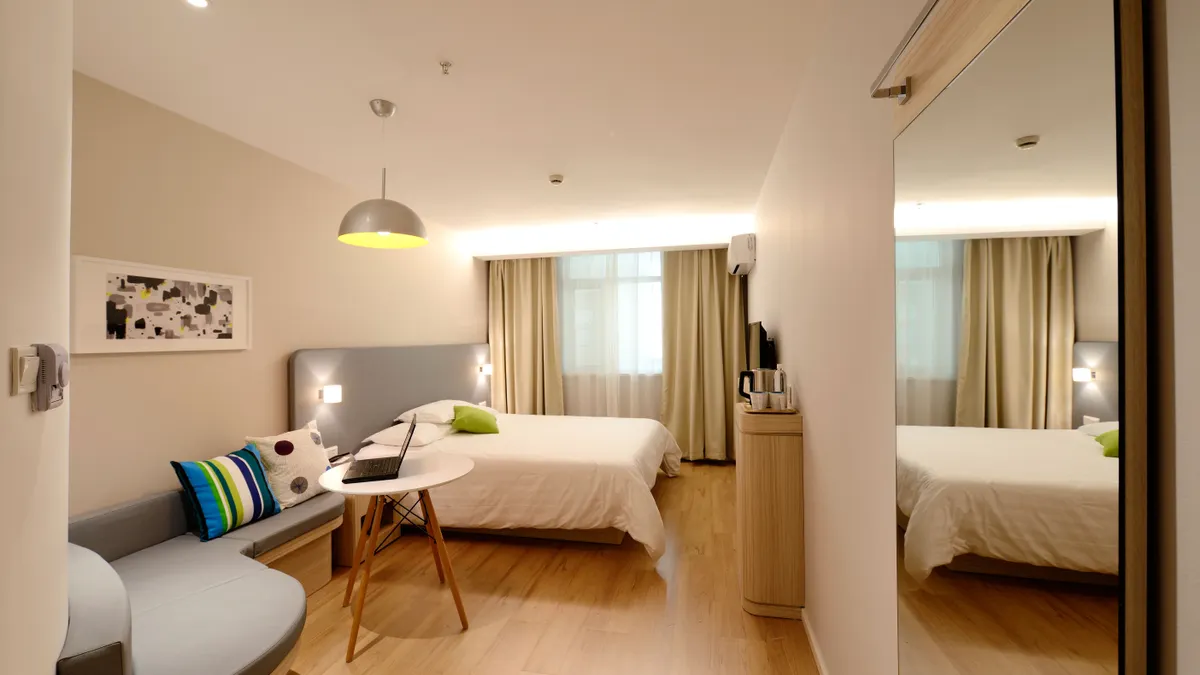 Modern hotel room with bed, sofa, mirror, and table